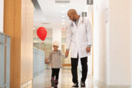 Doctor walking with pediatric cancer patient down hallway