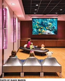 Children sit in a colorful theater room and watch a movie.